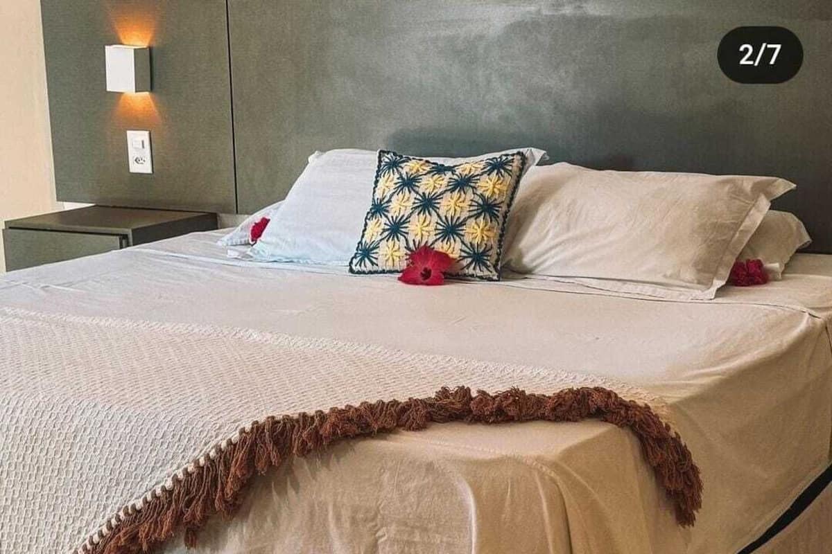 Ein ordentlich bezogenes Bett mit weißer Bettdecke, einem Zierkissen und einem braunen, fransigen Detail.