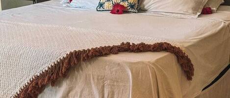 A neatly made bed with a white bedspread, a decorative pillow, and a brown fringe detail.
