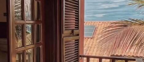 A balcony with a wooden railing, a red wall, and a view of palm trees.