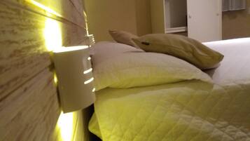 Una cama con un edredón amarillo acolchado y dos almohadas, una lámpara de noche y un cabecero de madera.