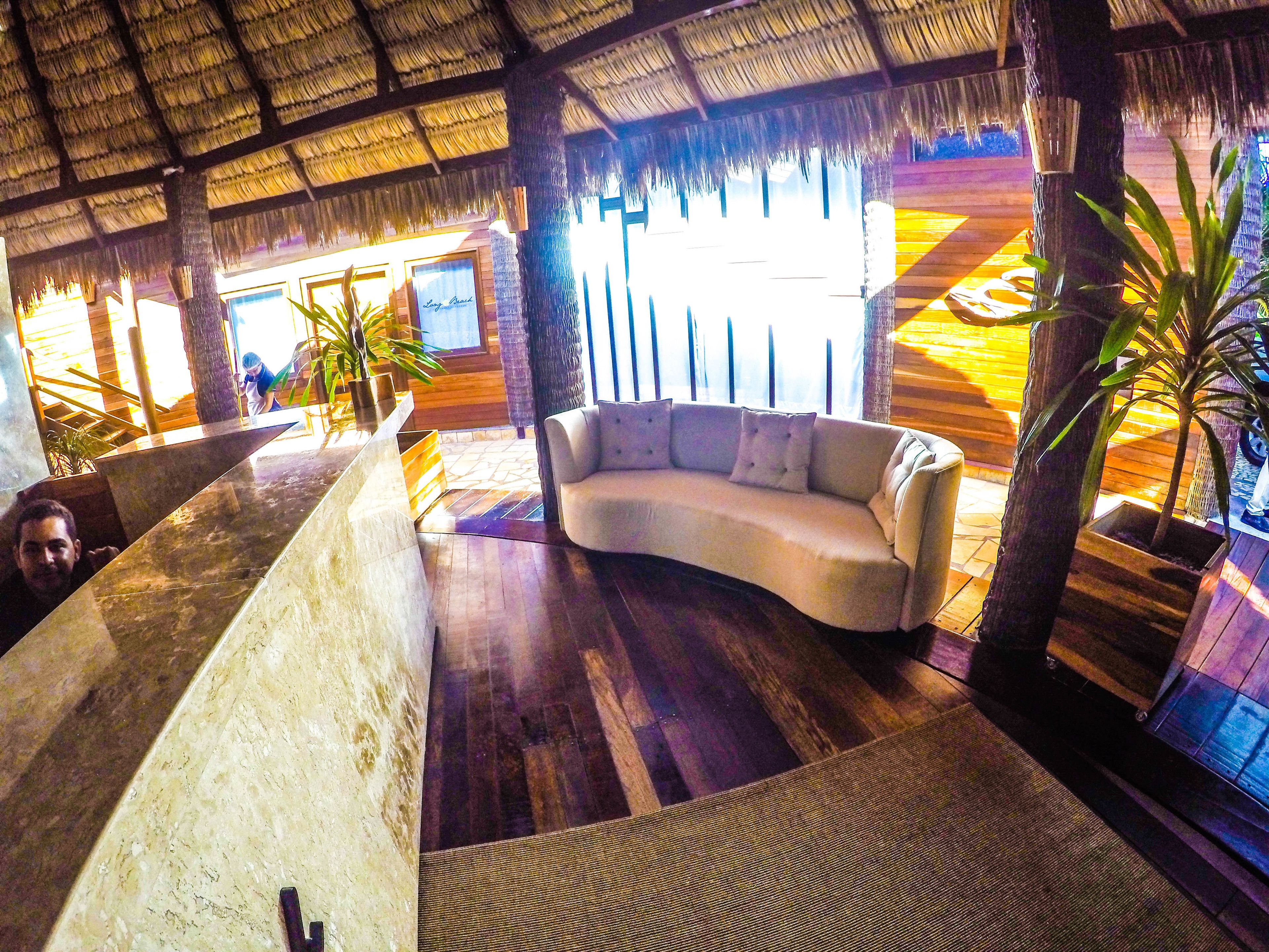 Una habitación con un sofá blanco curvo, techo de paja, piso de madera y plantas en macetas.