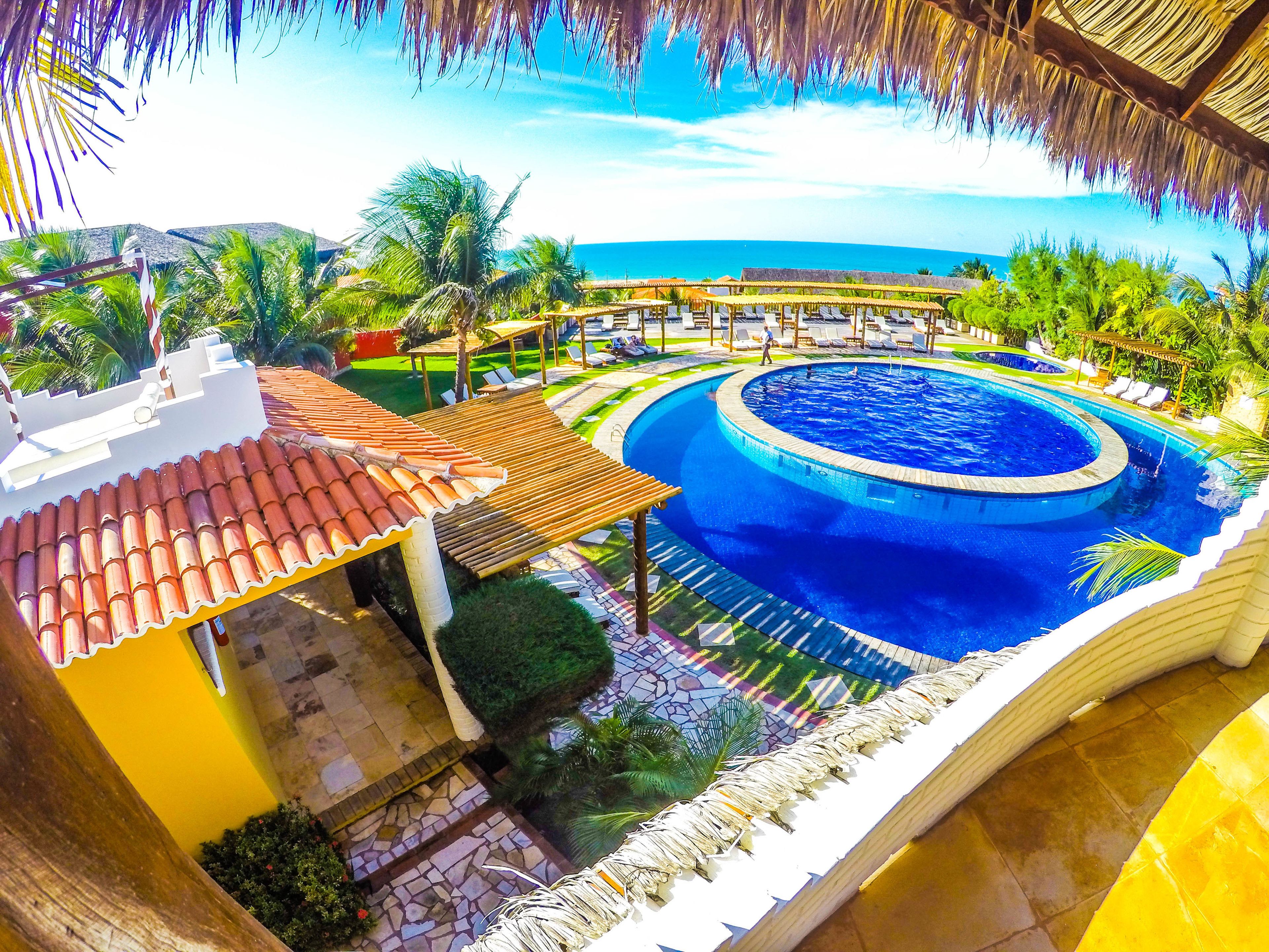 A resort with a circular pool, palm trees, and a view of the ocean.
