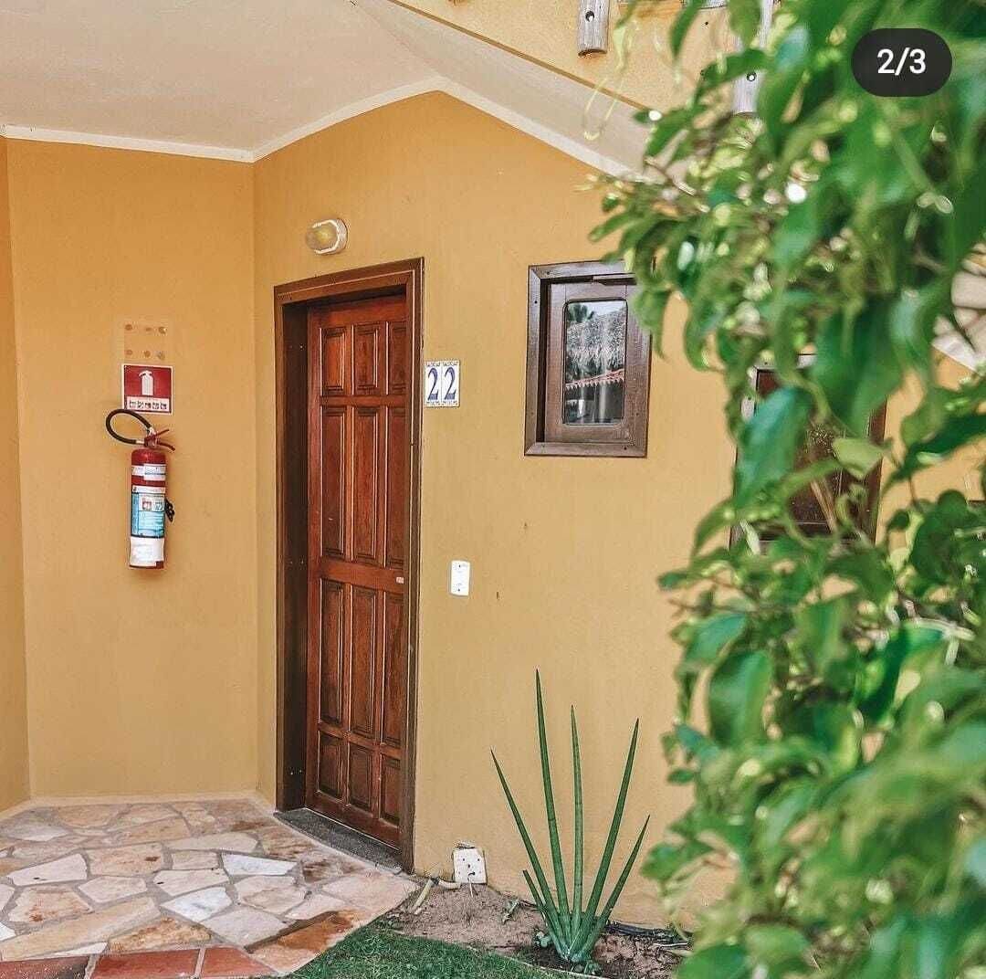 A building entrance with a wooden door, a fire extinguisher, a number sign, and a framed picture on the wall.