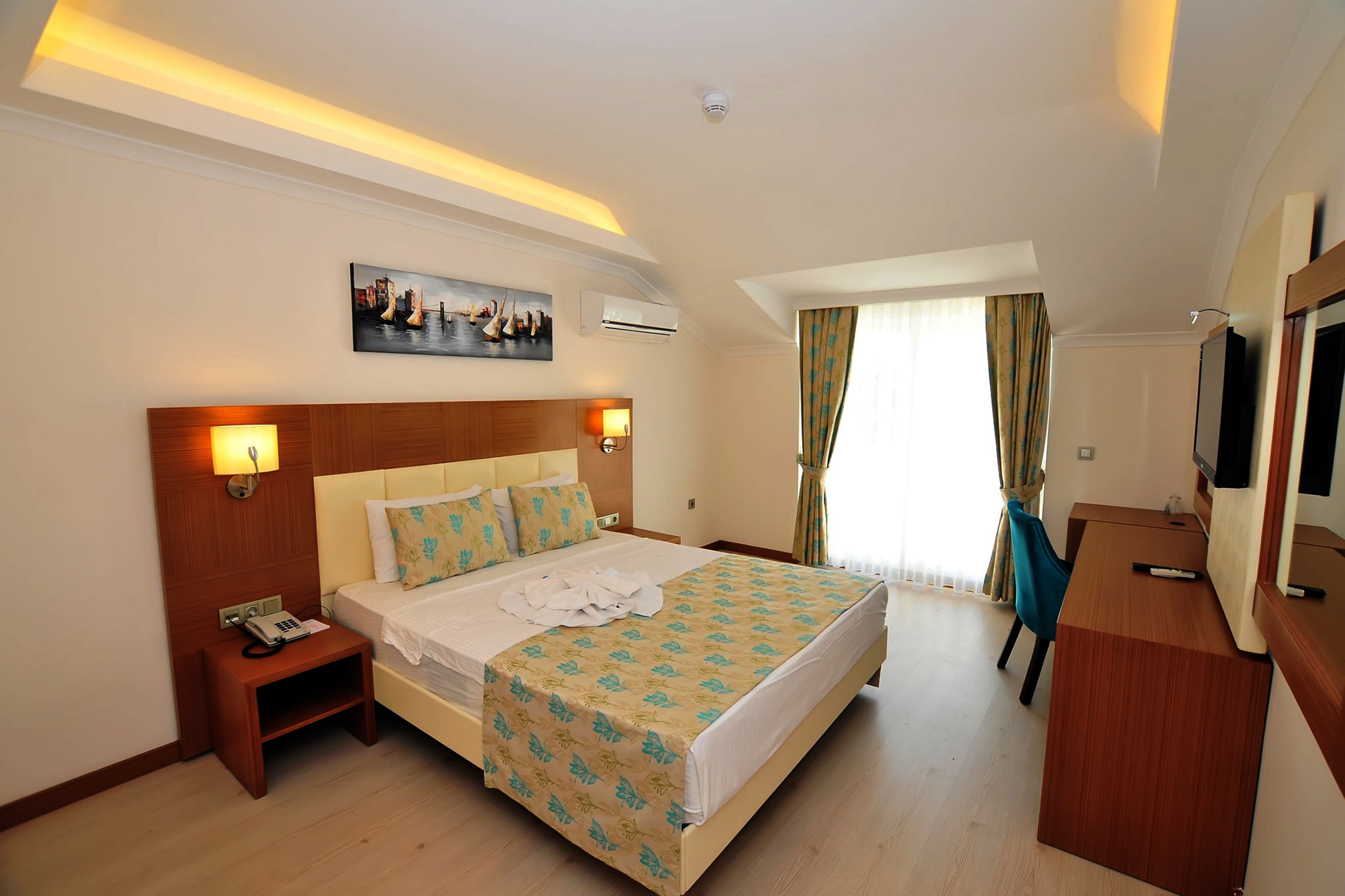 Habitación de hotel con cama, mesita de noche, lámpara, aire acondicionado y escritorio con silla.