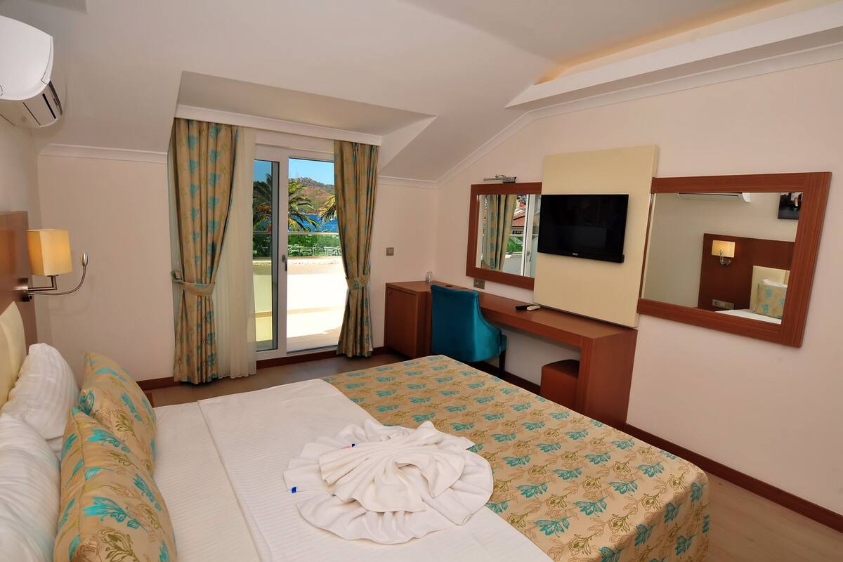 A hotel room with a bed, a desk, a TV, and a large window with curtains.