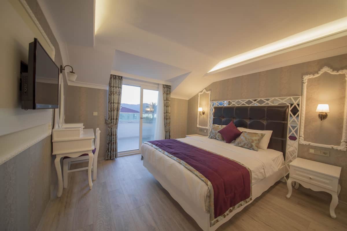 A hotel room with a bed, a desk, a chair, a television, and a balcony with curtains.