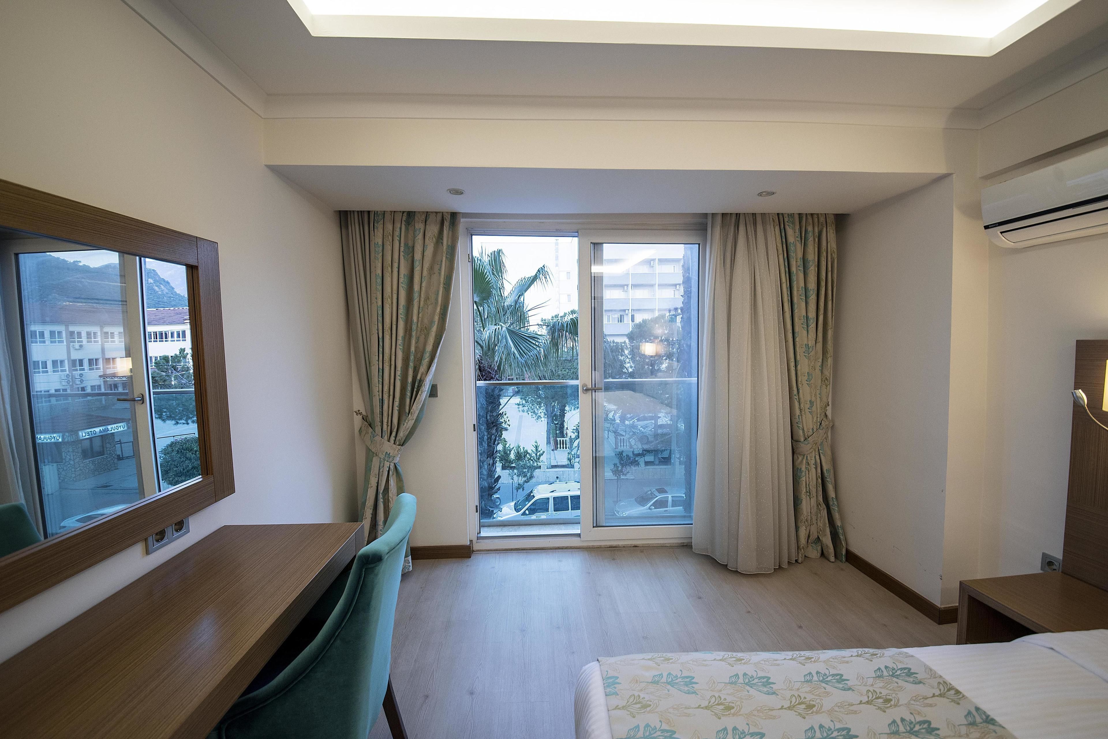 Quarto de hotel com uma janela grande, uma mesa, uma cama e um aparelho de ar condicionado.