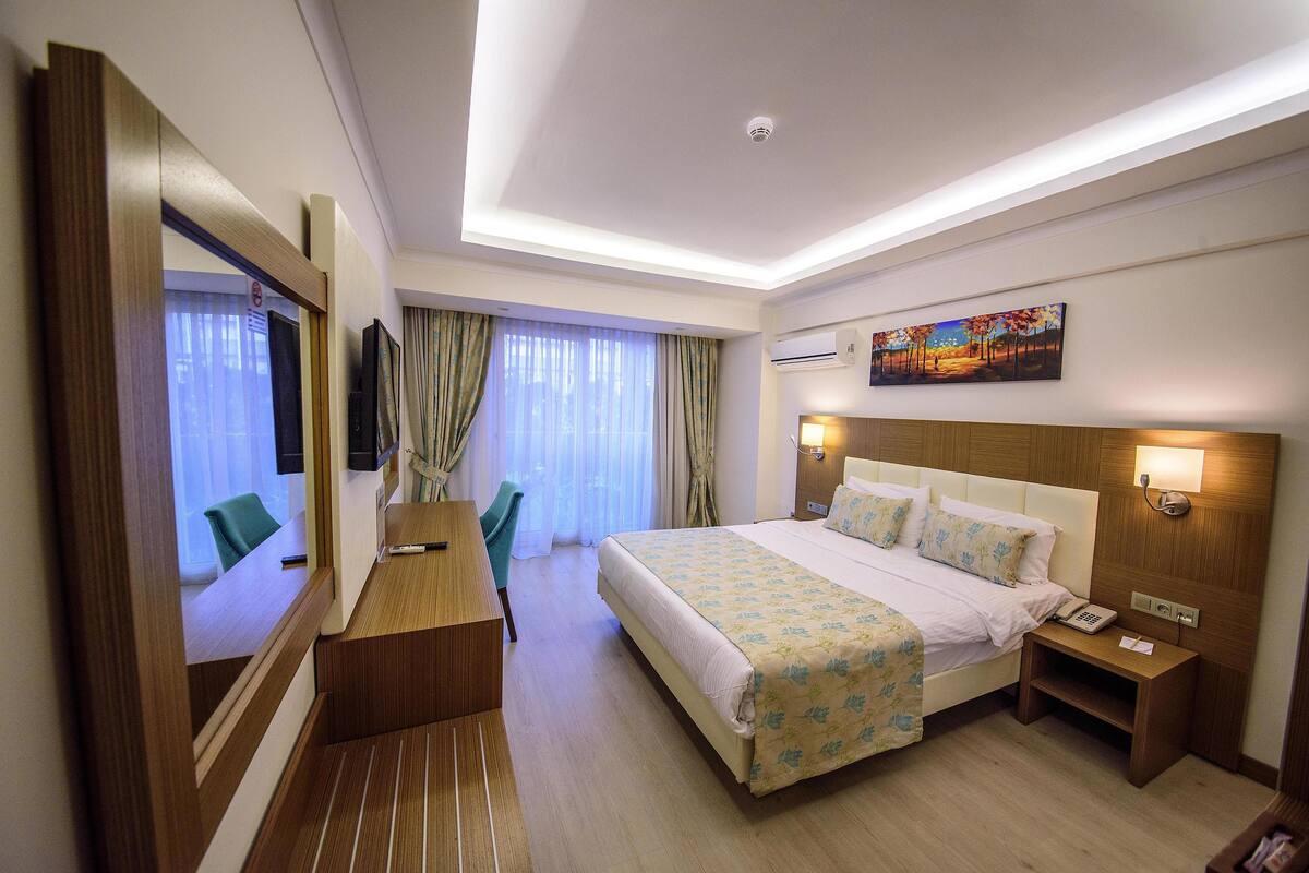 A hotel room with a large bed, a desk, a chair, a TV, and a painting on the wall.