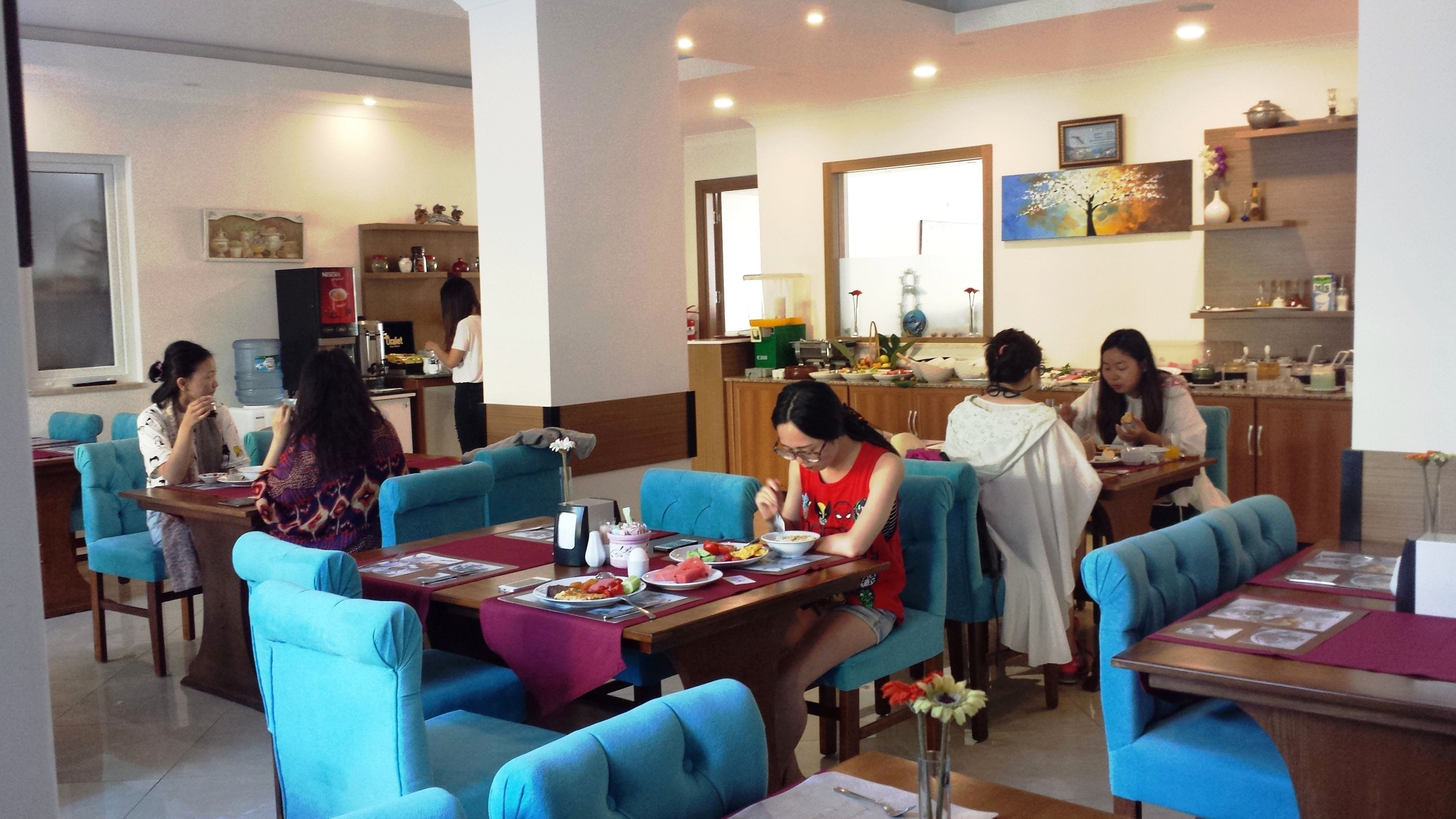 A dining area with blue upholstered chairs and tables, a kitchen area with a water dispenser, and a dining table with plates of food.