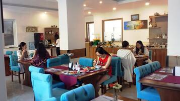 A dining area with blue upholstered chairs and tables, a kitchen area with a water dispenser, and a dining table with plates of food.
