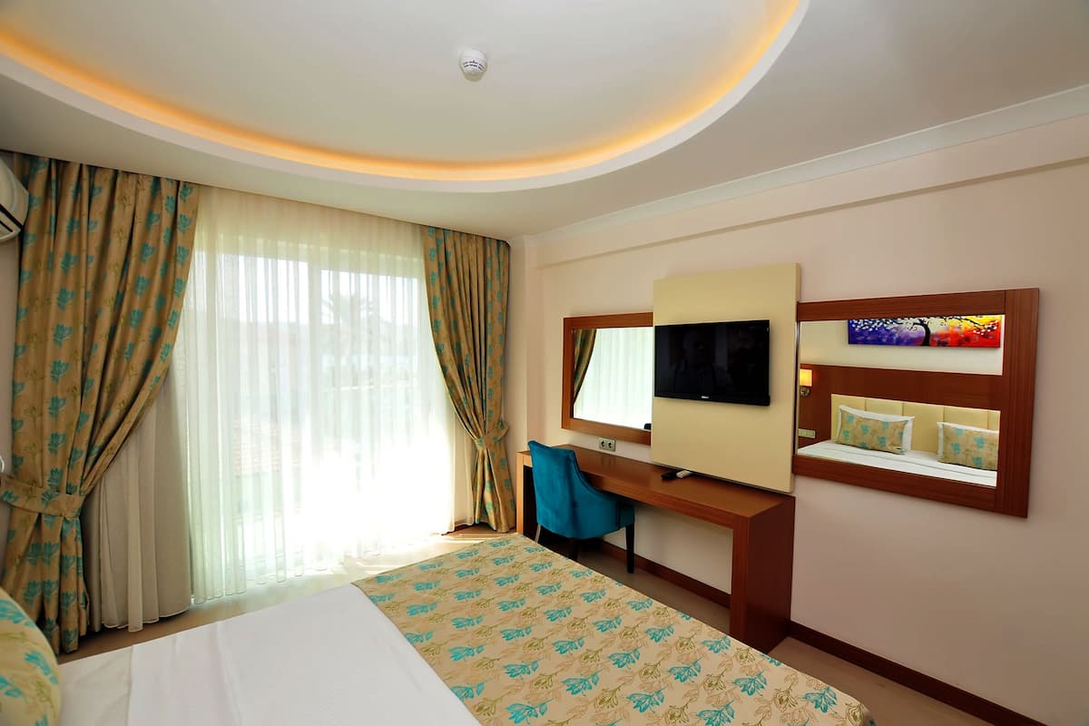 A hotel room with a bed, a desk with a computer, a TV, and a window with curtains.