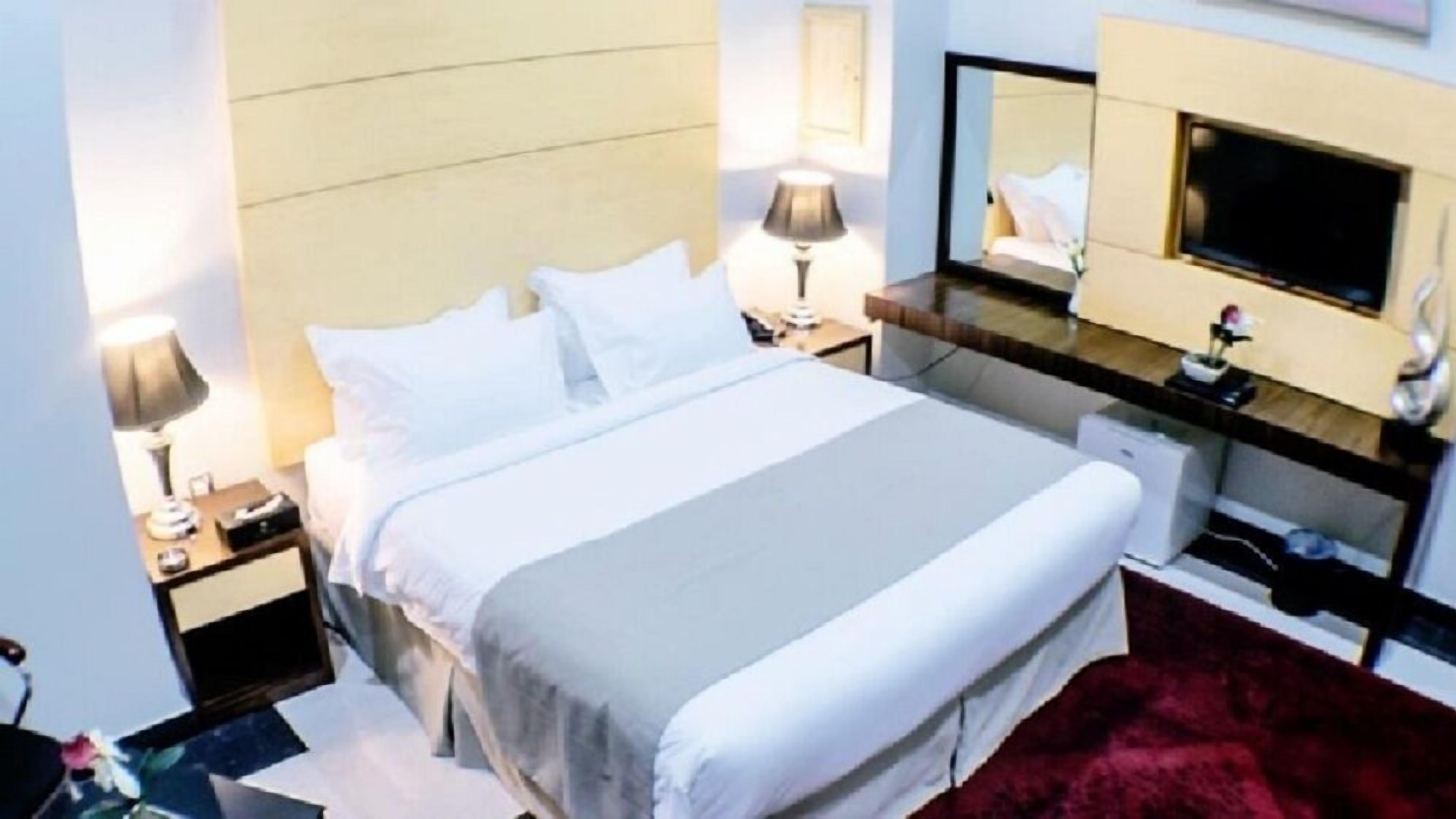 A hotel room with a bed, nightstands, a TV, and a mirror.