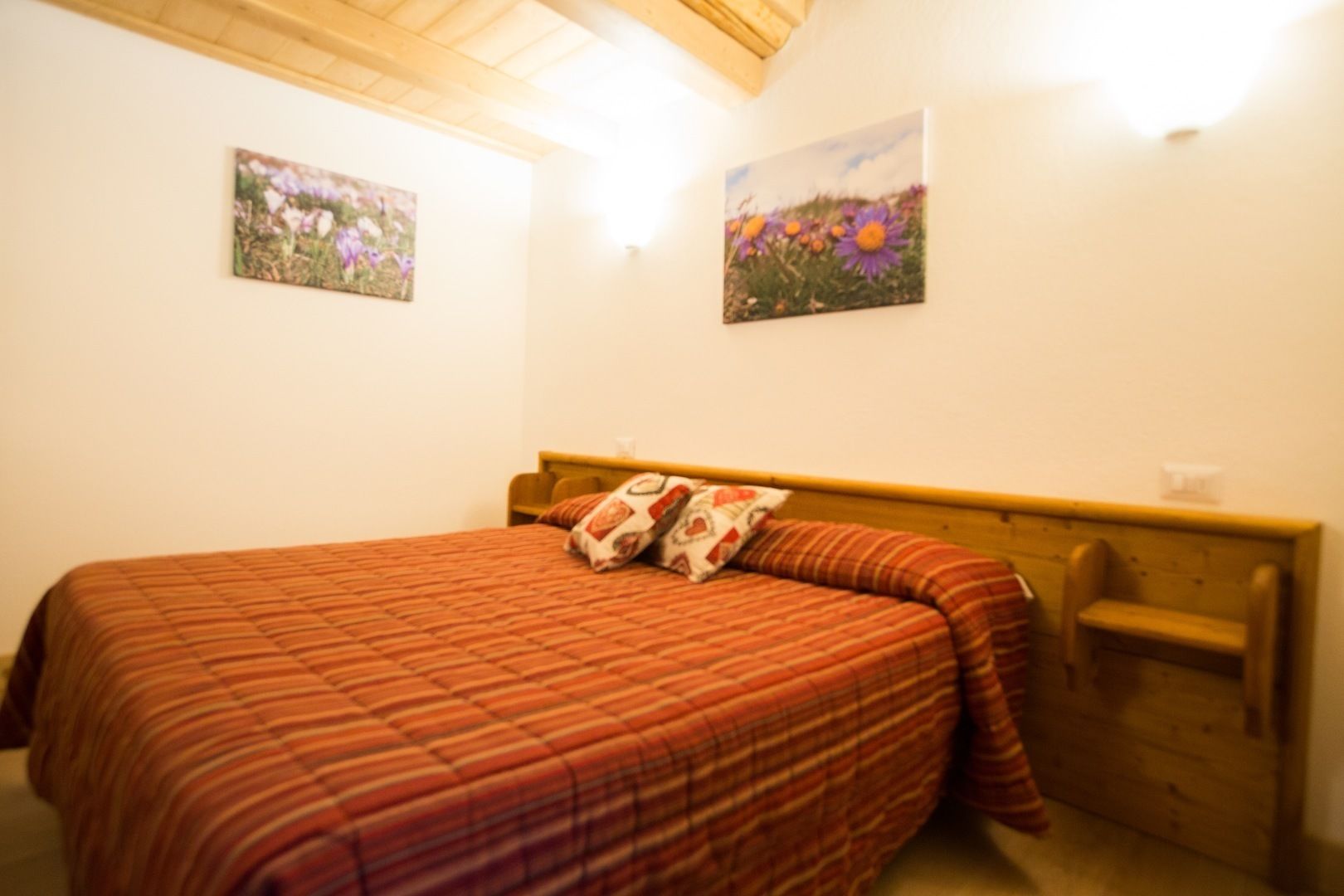 A bedroom with a bed, wooden headboard, and two wall-mounted paintings.