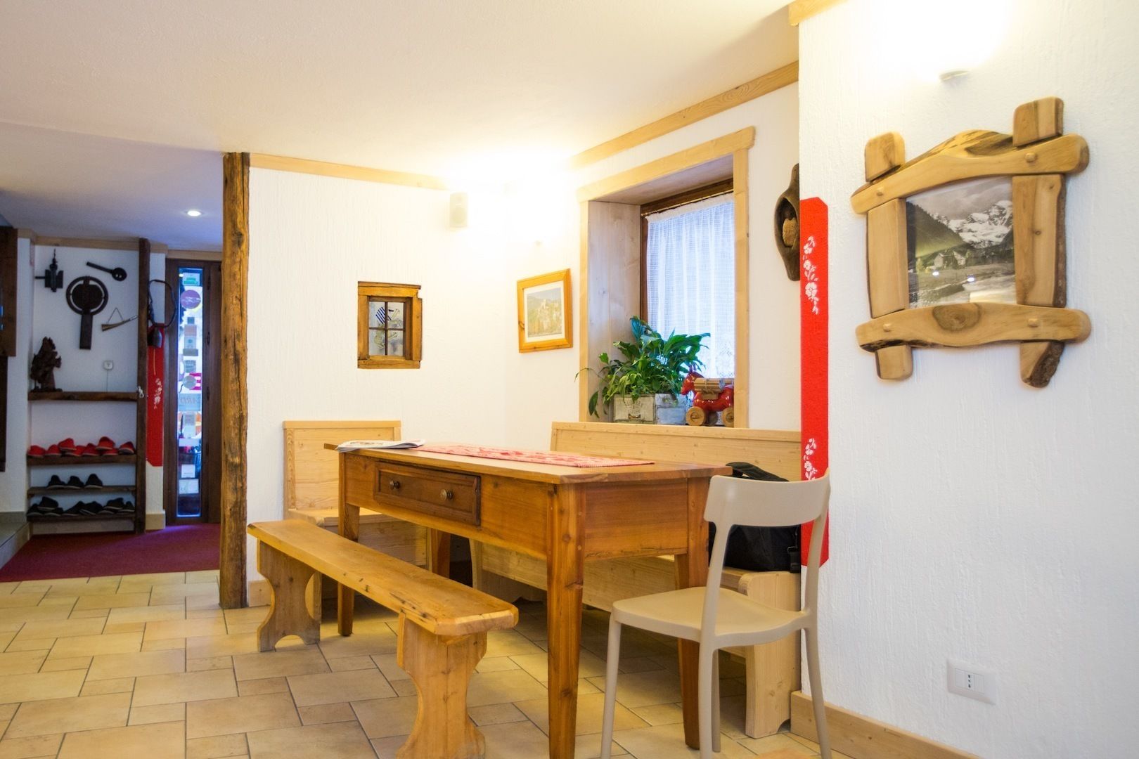 A room with a wooden desk, a chair, a bench, a window with a view, and a shelf with shoes.