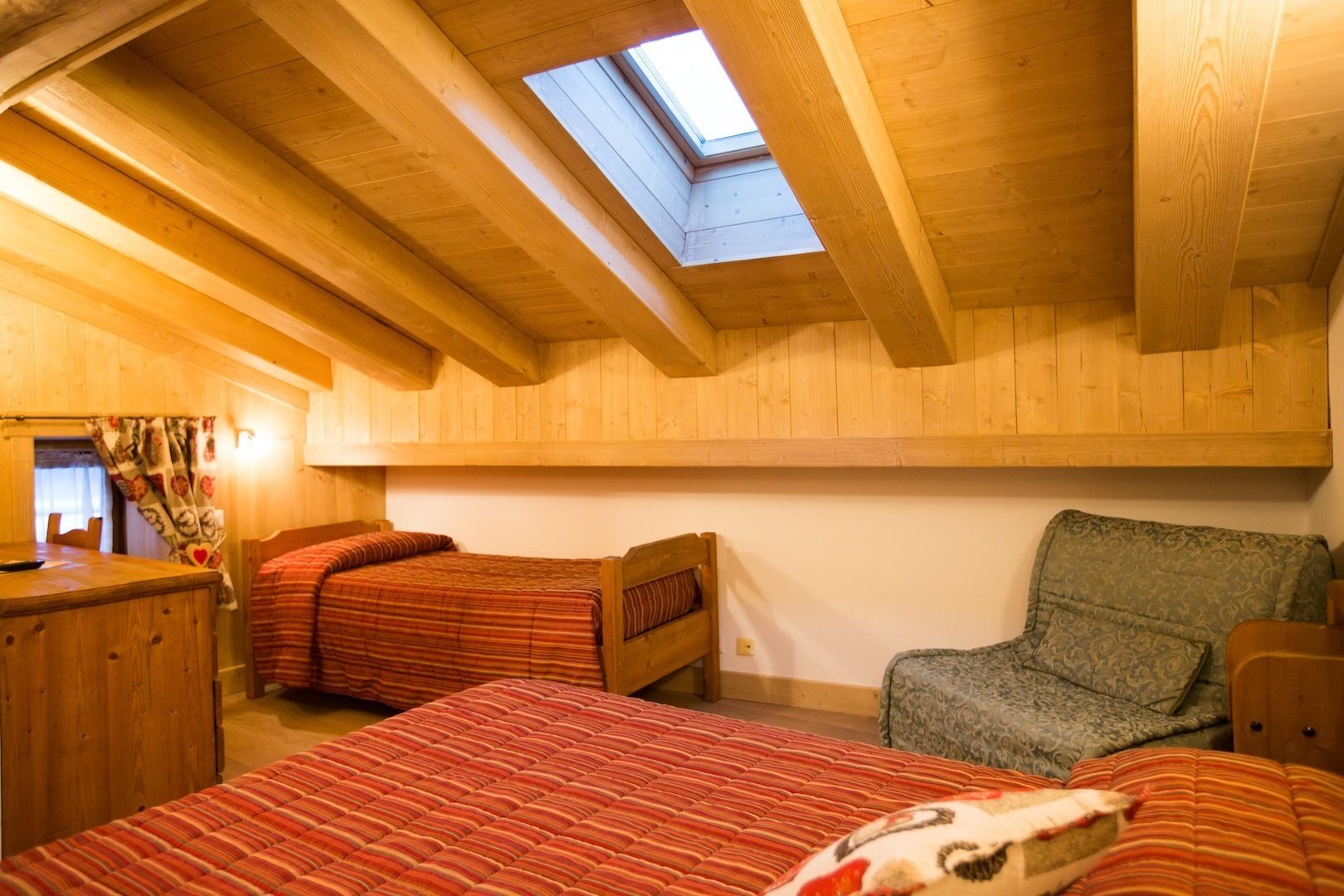 Quarto de sótão aconchegante com vigas de madeira, um claraboia, duas camas com roupa de cama listrada, uma cadeira e uma pequena mesa.