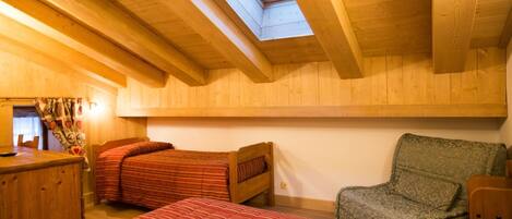 Quarto de sótão aconchegante com vigas de madeira, um claraboia, duas camas com roupa de cama listrada, uma cadeira e uma pequena mesa.