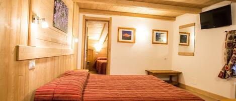 A wooden room with two beds, a TV, and framed pictures on the wall.