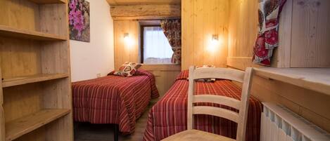 Une chambre confortable de style cabane, avec deux lits, des étagères en bois, une chaise et une fenêtre avec des rideaux.