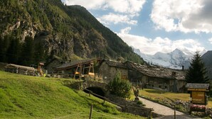 A mountain village with rustic buildings, a small bridge, and a sign for a restaurant. - La Barme (Cogne)