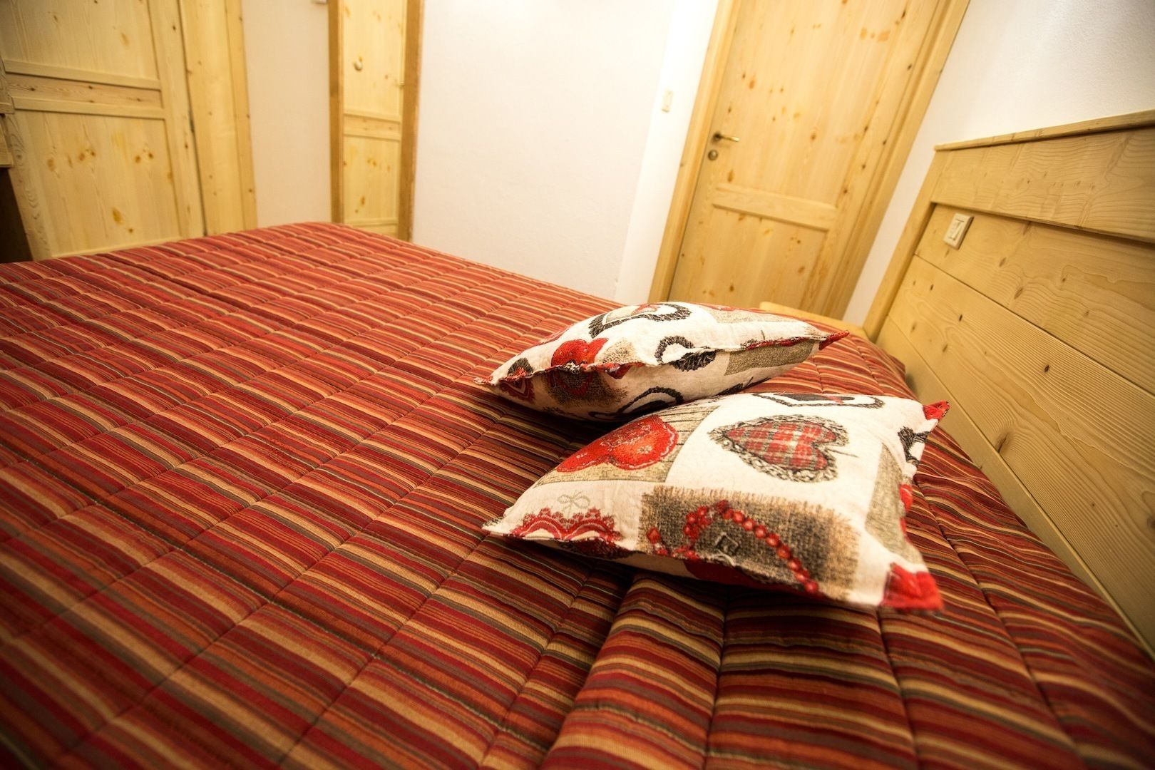 Cama com colcha listrada em vermelho e castanho e duas almofadas decorativas.