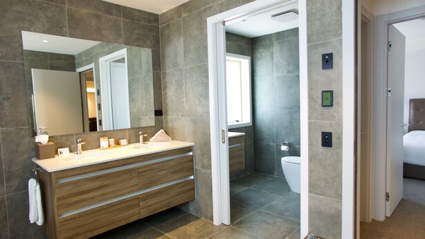 A modern bathroom with a wooden vanity, a large mirror, and a separate toilet area. - Regal Palms Resort (Rotorua)