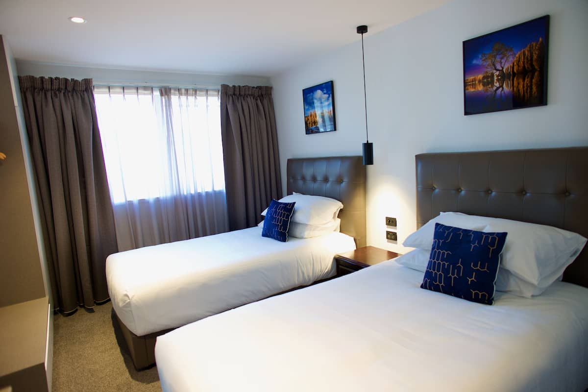 Une chambre d’hôtel avec deux lits, une grande fenêtre avec des rideaux et un tableau au mur.