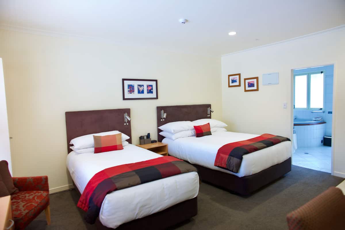 Une chambre d’hôtel avec deux lits, une chaise, une petite table et une salle de bain visible, équipée d’une baignoire.