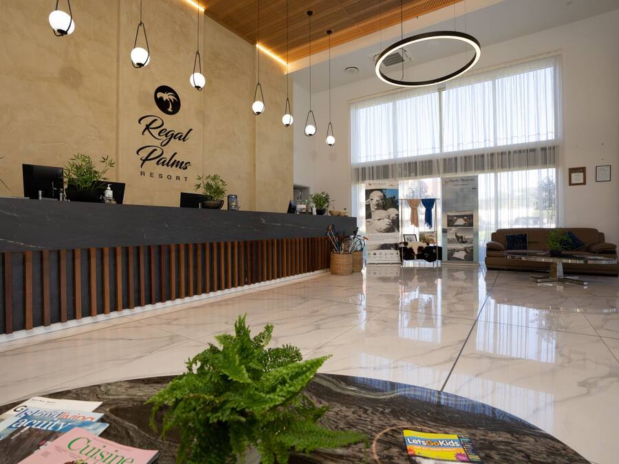 Um hall amplo com balcão de recepção, iluminação moderna e uma grande janela que proporciona luz natural.