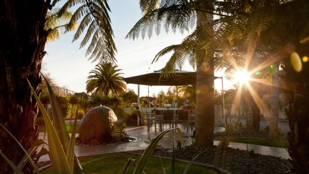 A patio area with outdoor seating, palm trees, and a pergola structure. - Regal Palms Resort (Rotorua)