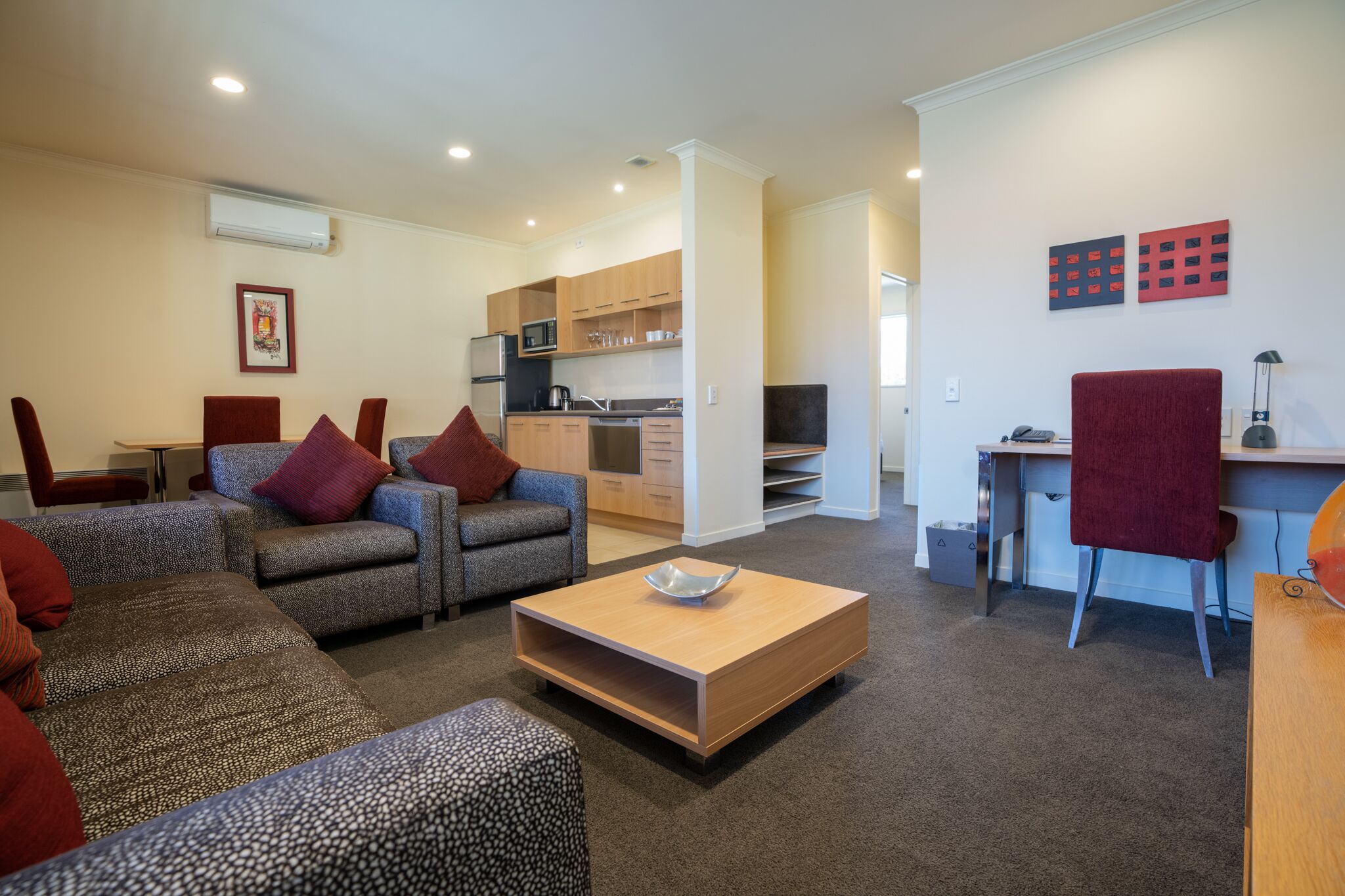 A modern living room with a sofa set, a coffee table, and a kitchen area visible in the background.