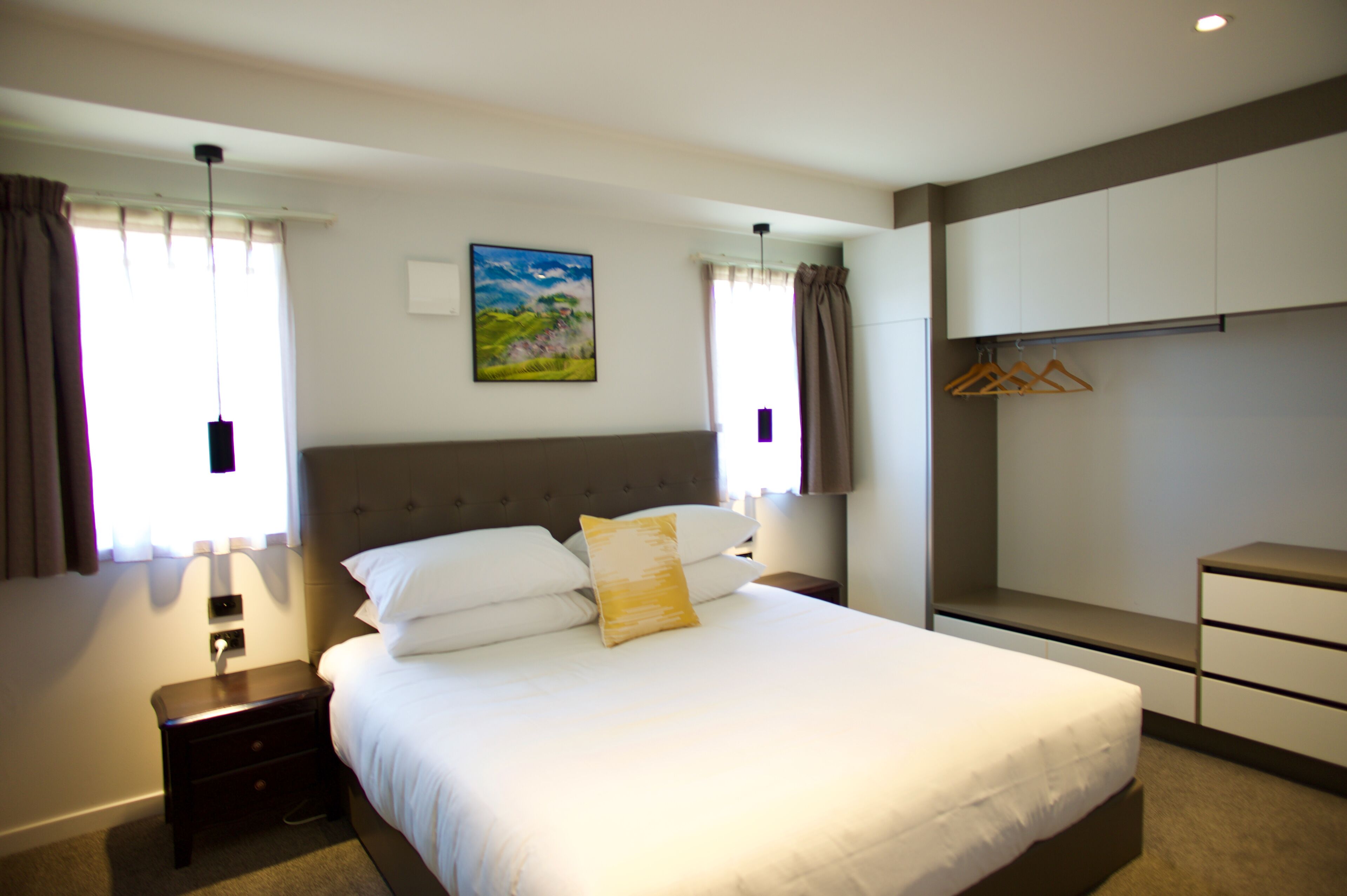 A hotel room with a large bed, bedside tables, a wardrobe, and a painting on the wall.