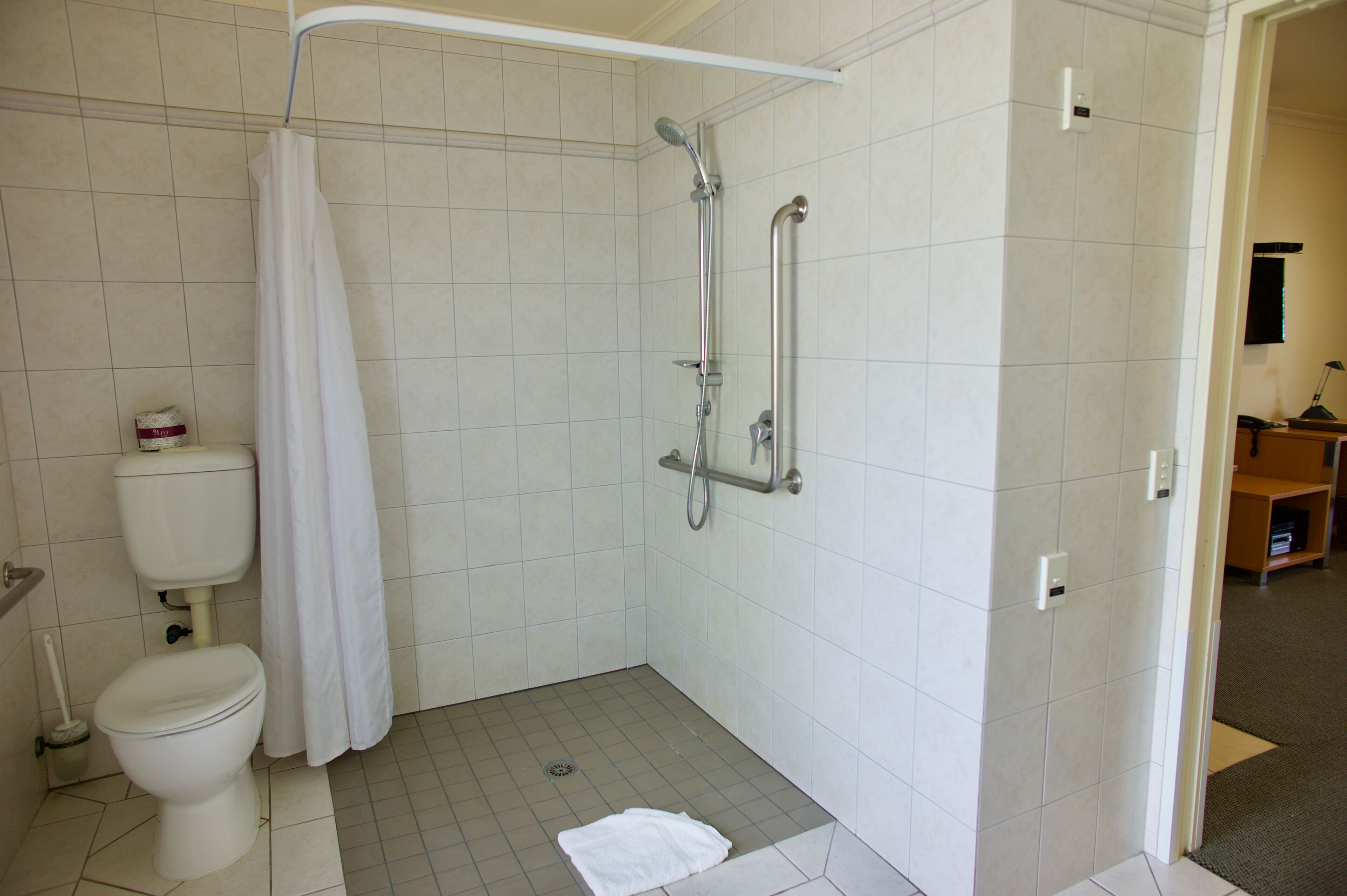 A bathroom with a shower, toilet, and a towel on the floor.