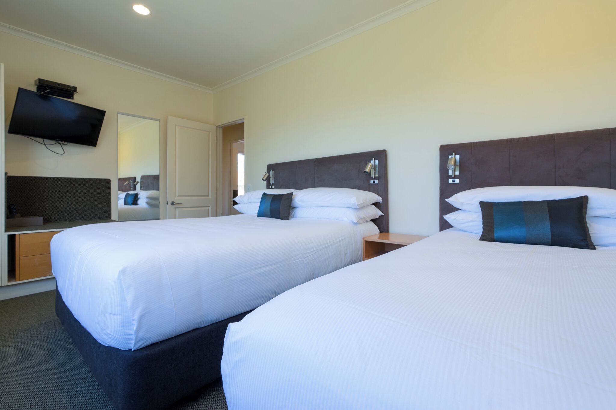 Une chambre d’hôtel avec deux lits, un téléviseur fixé au mur et une porte donnant sur la salle de bain.