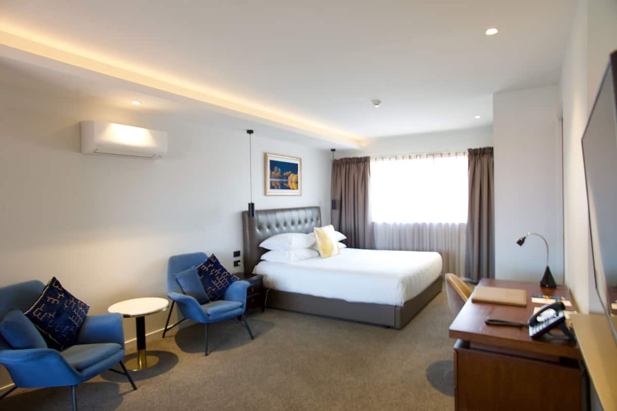 Une chambre d’hôtel avec un lit, deux fauteuils, un bureau et une petite table.