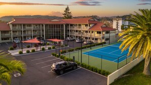 A hotel with a tennis court, multiple parking spaces, and a parking lot with several cars. - Regal Palms Resort (Rotorua)