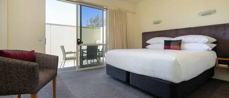 Une chambre d’hôtel avec un grand lit, une chaise, une petite table et une porte-fenêtre coulissante donnant sur l’extérieur.
