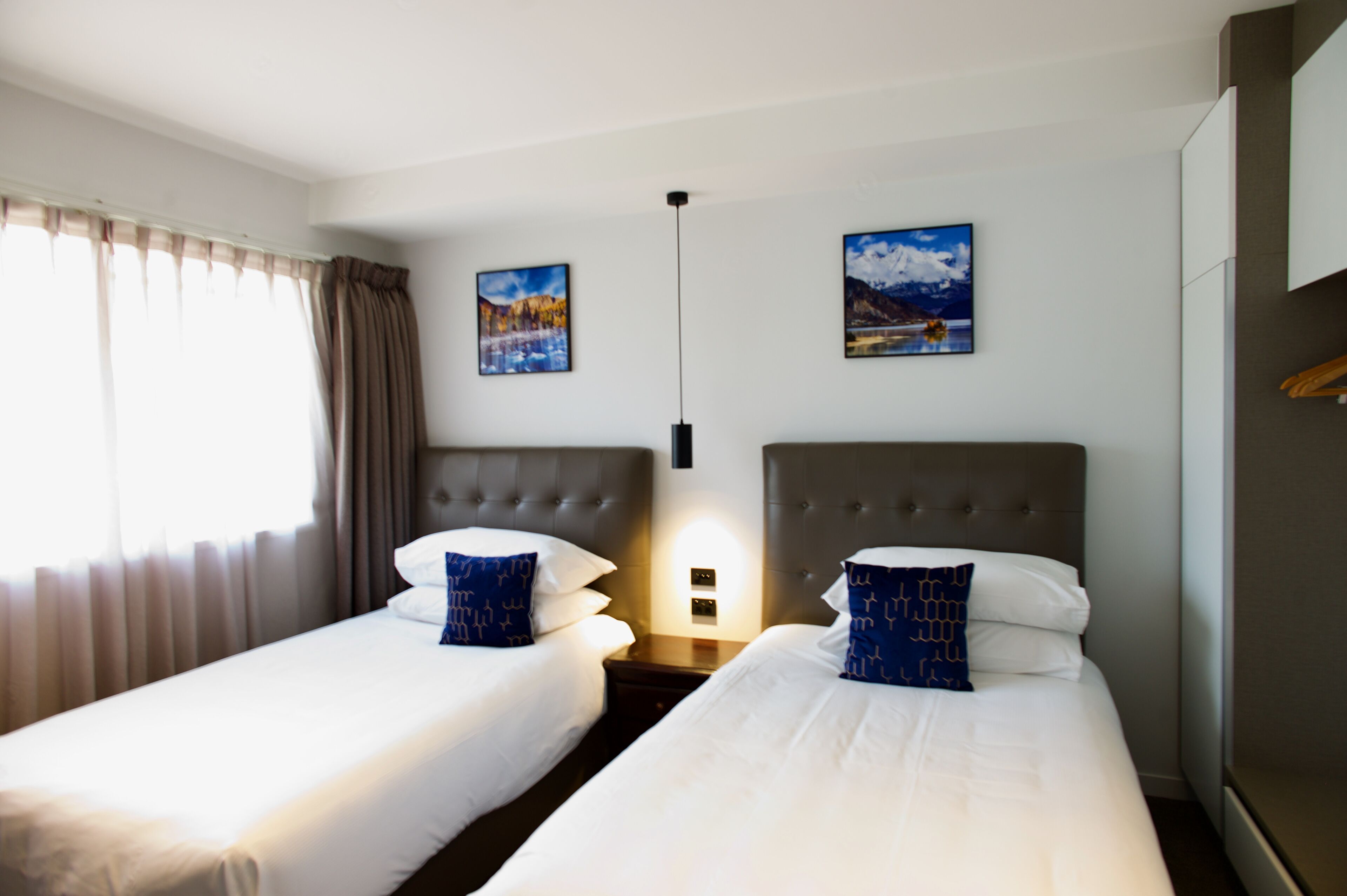 Een hotelkamer met twee enkele bedden, een nachtkastje, een wandlamp en twee ingelijste foto's aan de muur.