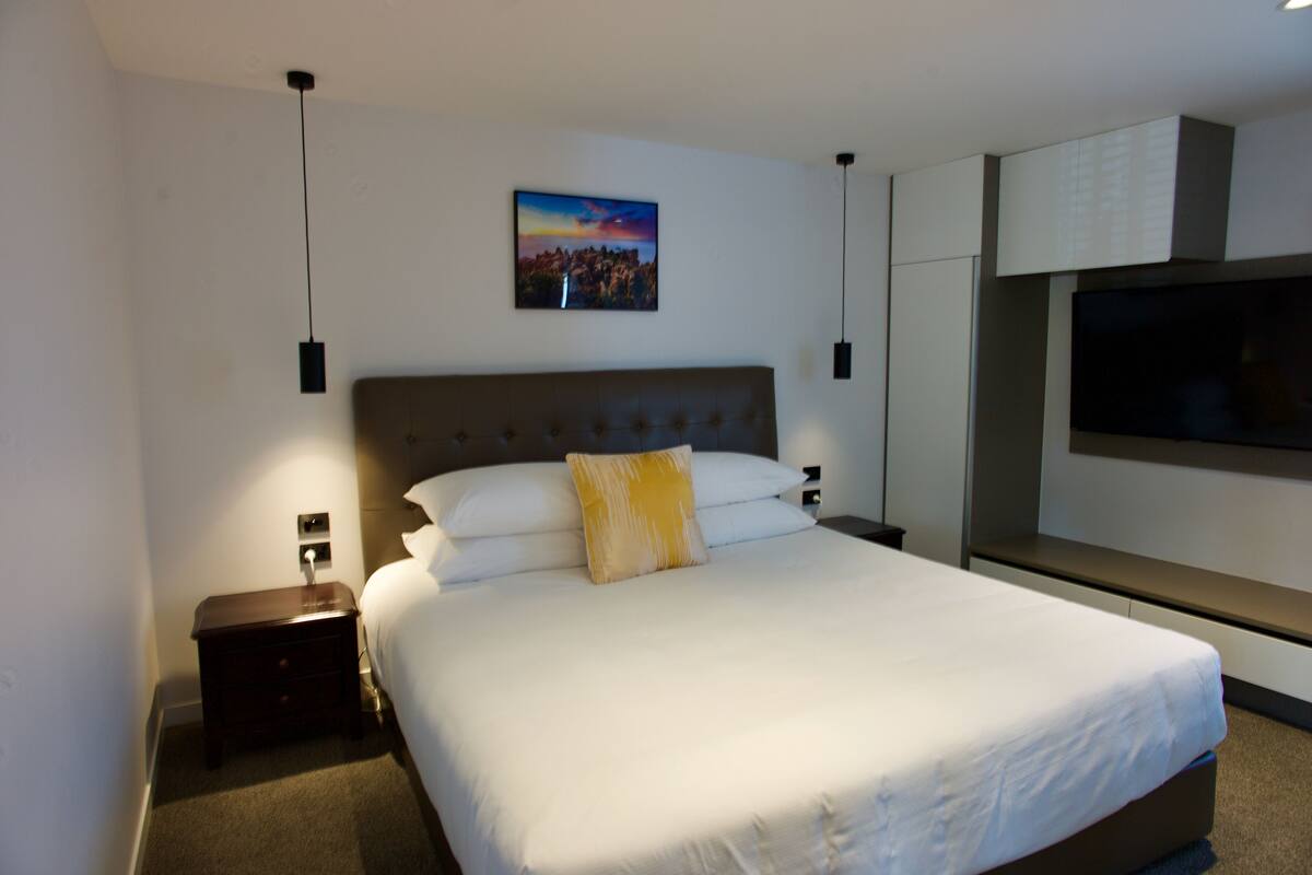 Une chambre d’hôtel moderne avec un grand lit, une table de chevet, une télévision et un tableau au mur.