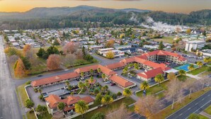 An aerial view of a residential area with multiple buildings, roads, and a large industrial facility emitting smoke in the background. - Regal Palms Resort (Rotorua)