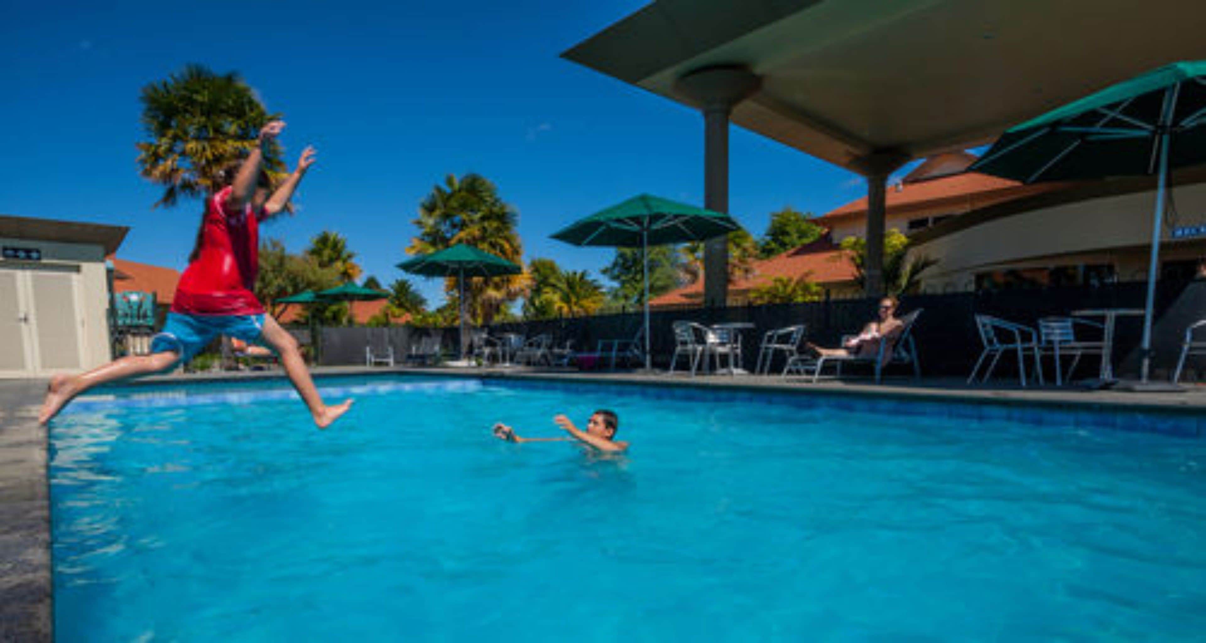 Piscina com pessoas brincando, guarda-sóis e espreguiçadeiras.
