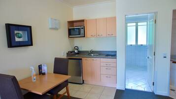 A compact kitchen with a microwave, sink, and dishwasher. There is a dining table with chairs and a framed picture on the wall.