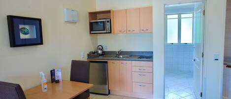 A compact kitchen with a microwave, sink, and dishwasher. There is a dining table with chairs and a framed picture on the wall.