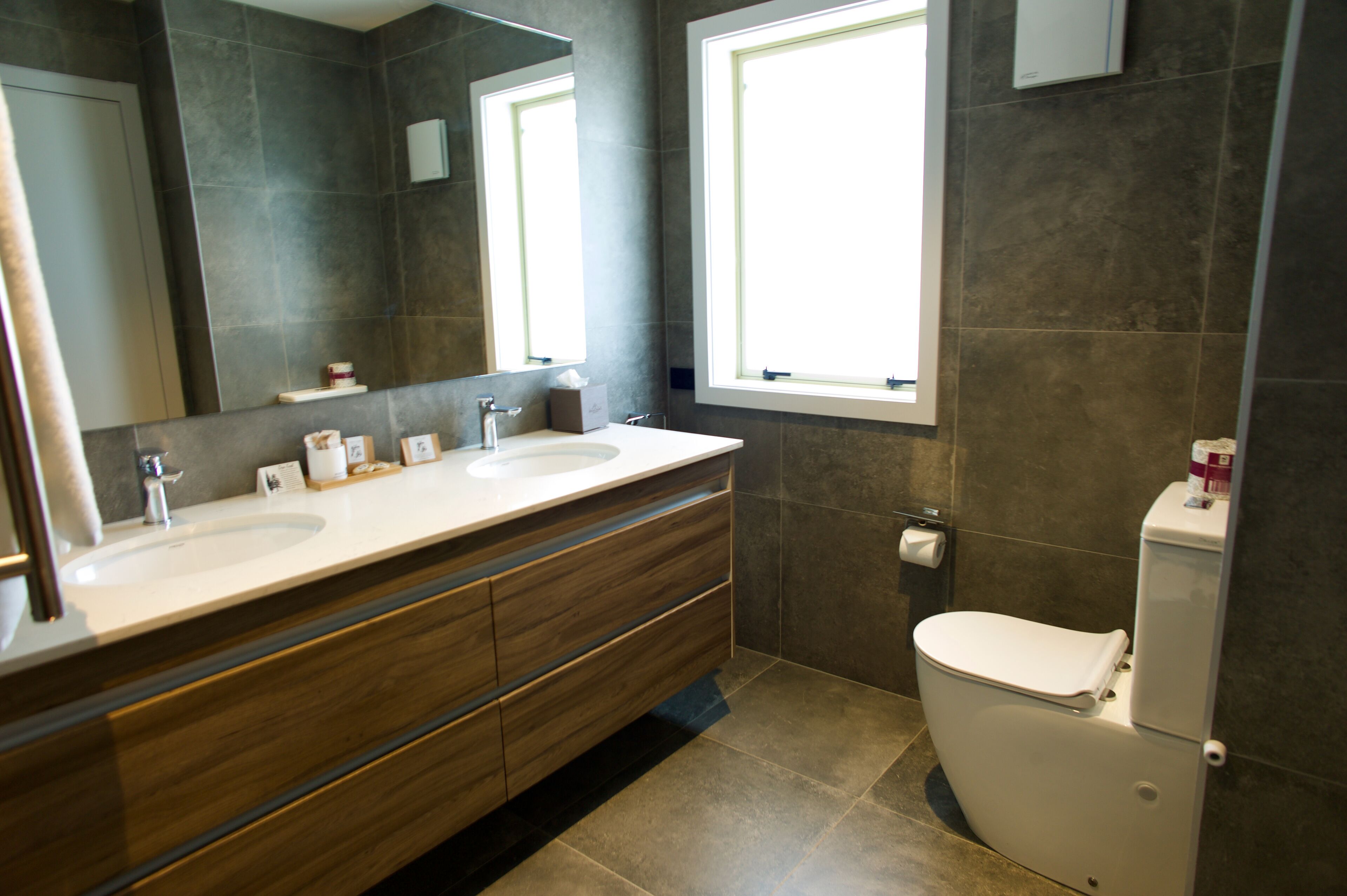 A modern bathroom with two sinks, a large mirror, and a toilet.