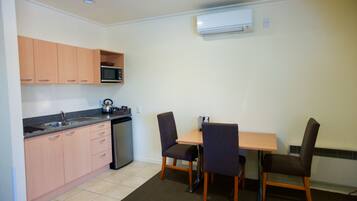 A compact kitchen with a microwave, sink, and cabinets. There is a small dining table with two chairs.