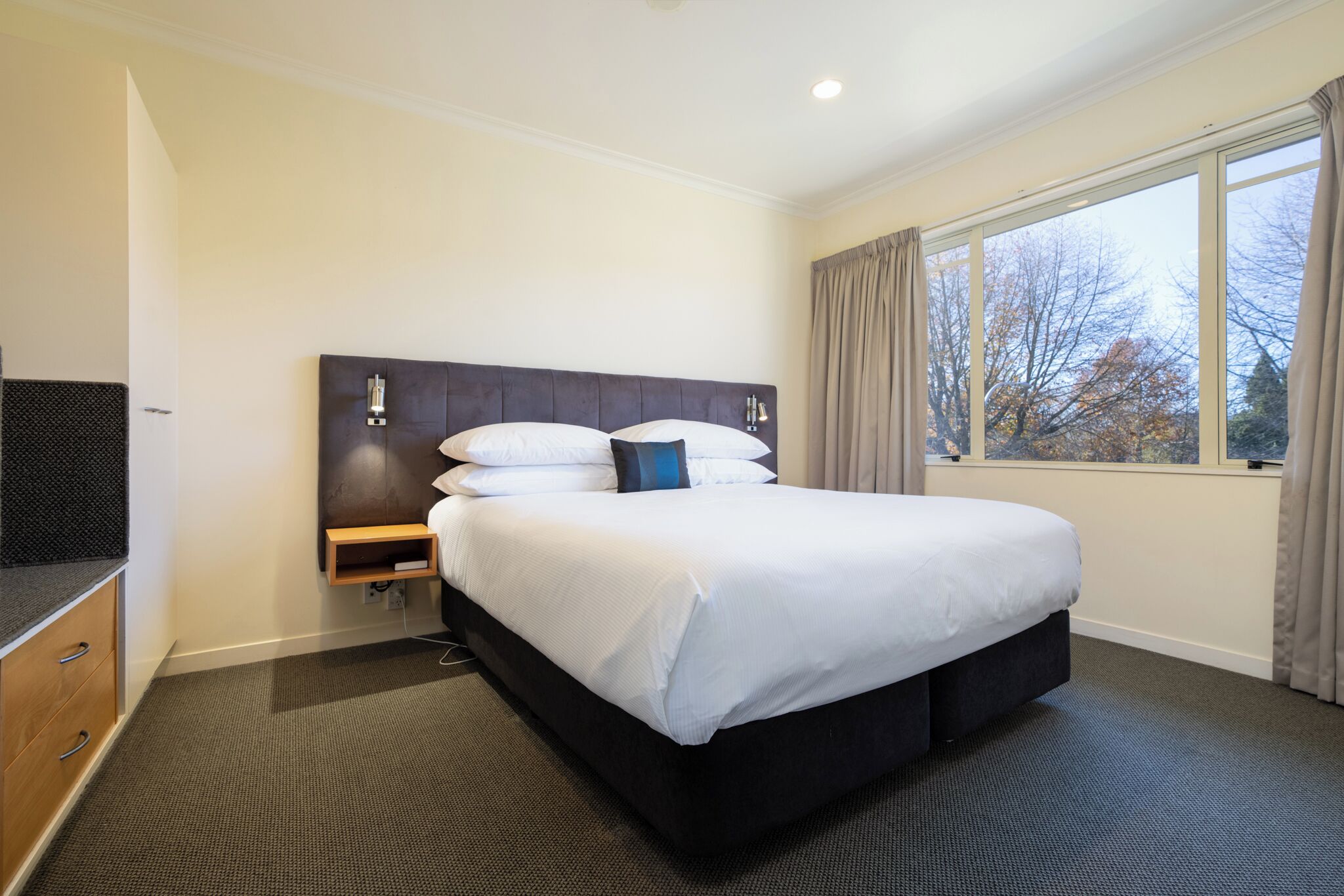 Habitación de hotel con una cama grande, una mesita de noche, un televisor de pantalla plana y una ventana con cortinas.