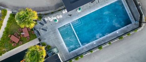 An aerial view of a hotel with a rectangular pool, lounge chairs, and palm trees.