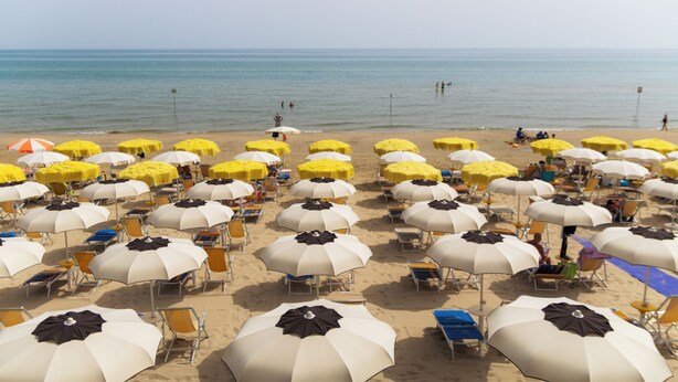 A beach with rows of umbrellas and chairs, some with people under them. - Felicioni (Pineto)