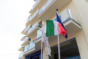 Un edificio de varios pisos con balcones e izado de múltiples banderas.