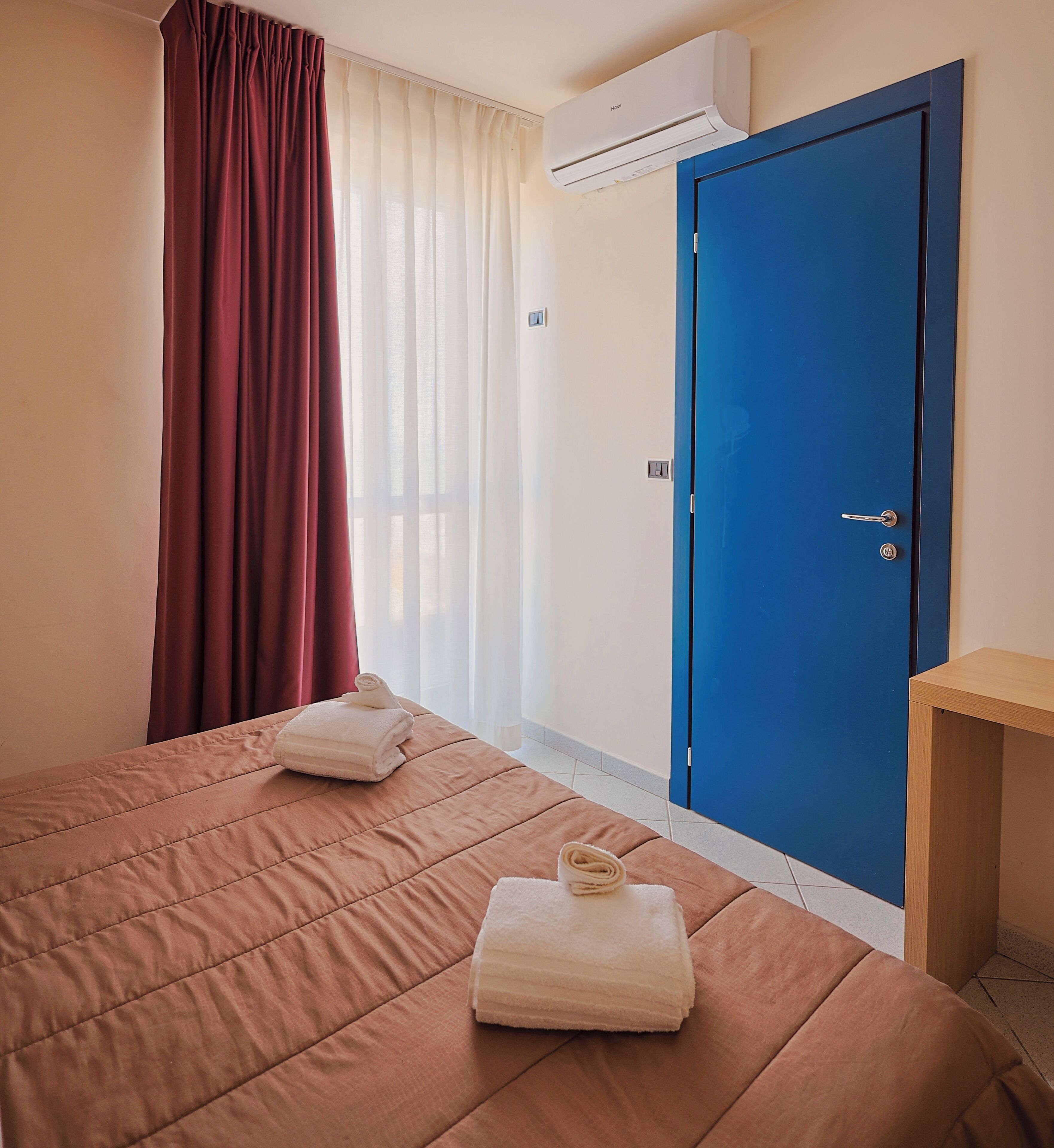 A hotel room with a bed, a blue door, and an air conditioning unit.
