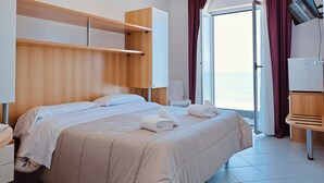 A hotel room with a bed, a wooden headboard, a desk, a chair, a TV, and a view of the sea. - Felicioni (Pineto)